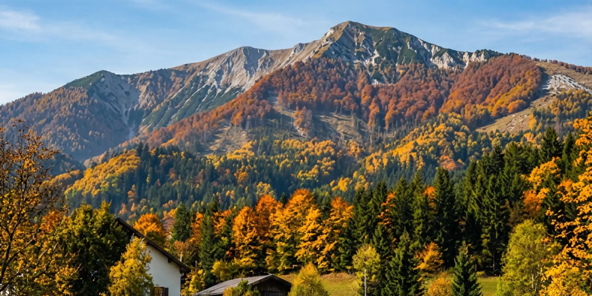 Der Ötscher im Herbst, davor die bunten Wälder und die Dächer von Lackenhof