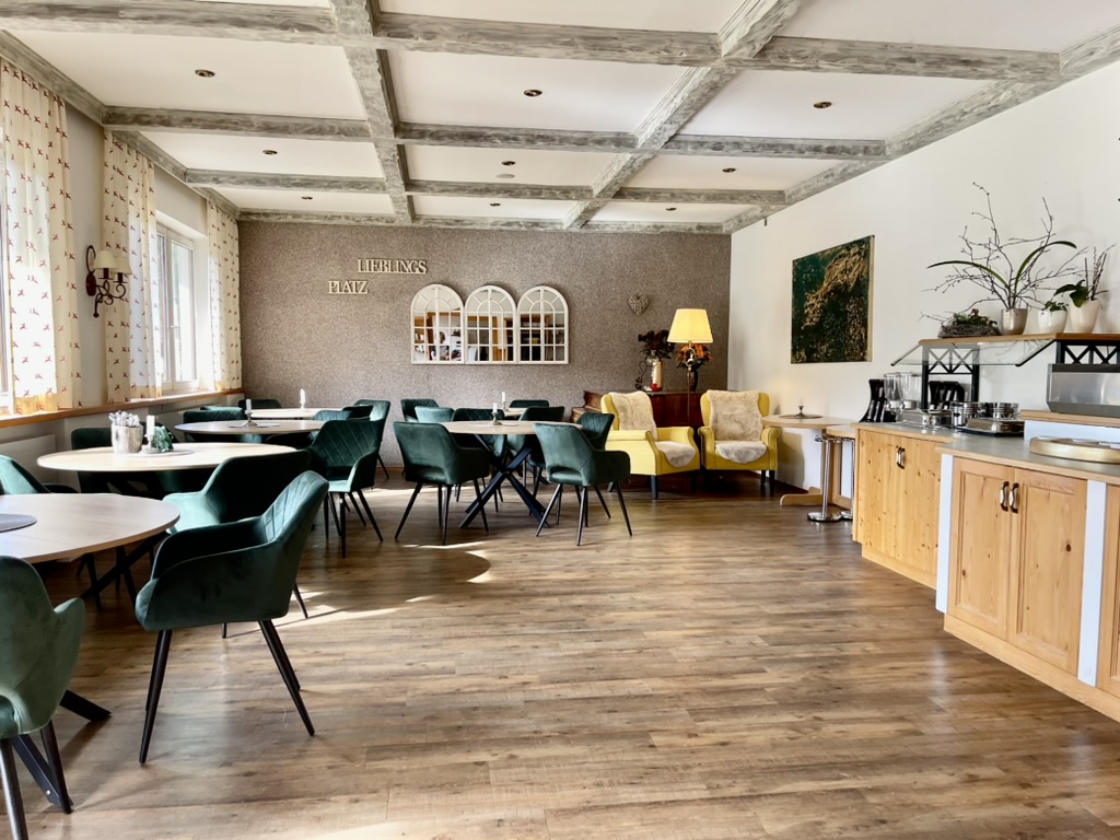 Heller Speisesaal mit runden Tischen, grünen Stühlen und Holzboden